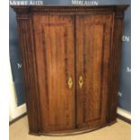 A late George III oak bow fronted hanging corner cupboard,