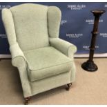 A modern pale green upholstered wing back scroll arm chair on turned legs to brass caps and castors,