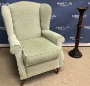 A modern pale green upholstered wing back scroll arm chair on turned legs to brass caps and castors,