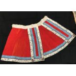 A Chinese red finely pleated silk skirt with blue and cream overlaid silk bands heavily embroidered