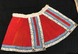 A Chinese red finely pleated silk skirt with blue and cream overlaid silk bands heavily embroidered