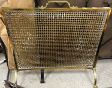 A brass fire guard with carrying handle, raised on Arts and Crafts style feet,