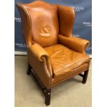 A modern brown leather upholstered and studded wing back scroll arm chair on square chamfered front