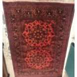 A Persian rug, the central panel set with two repeating flower head medallions on a dark red ground,