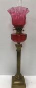 A Victorian brass corinthian column table lamp with cranberry glass reservoir and shade 83 cm high