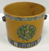 A 19th Century Chinese famille jaune cylindrical pot with twin mask side handle holders,