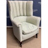 A circa 1900 upholstered barrel wing back armchair with scroll arms on cabriole front legs to brass