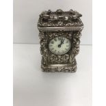 A French cast white metal cased miniature carriage clock with visible escapement and white circular