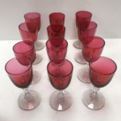 A collection of twelve cranberry glass wines with clear glass stems on circular feet,