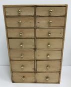 A pine table top chest of two banks of seven graduated drawers with brass knob handles 28 cm wide x