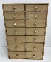 A pine table top chest of two banks of seven graduated drawers with brass knob handles 28 cm wide x