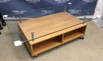 A modern glass top coffee table on a beech effect and tubular metal base and castors 135 cm x 75 cm