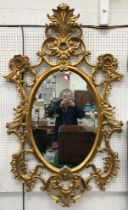 A Harrison & Gil carved gilt wall mirror with oval bevel edged plate, C scroll,