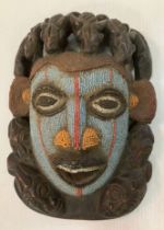 A carved wooden and turquoise and coral bead embellished mask,