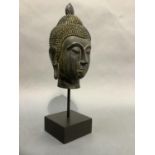 An ebonised bust of buddha, picked out in ochre, raised on a metal column and on square plinth base,