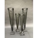 Two pairs of tall metal and glass flower vases of square tapered outline on domed bases, 65cm and