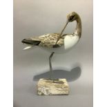 A carved and painted figure of a wading bird mounted on a washed wooden base