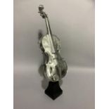 A white metal violin raised on an ebonised pedestal,62cm high