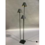 A triple standard lamp, the three graduated height column lamps each with black shade and on a