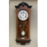 A small walnut wall clock having two part enamel dial with black Roma numerals and exposed pendulum,