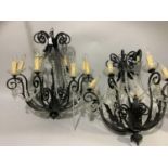 A pair of eight light chandeliers with black metal scrolling arms and leafage, glass sconces,