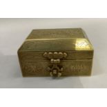 A Chinese brass box having a canted lid with strapwork hinges and lock all over engraved with