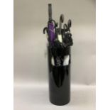 A black perspex umbrella stand by Kartel (at fault) containing a variety of umbrellas and walking