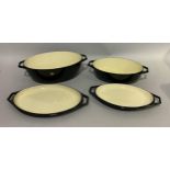 Two Le Creuset black and cream casserole dishes of graduated size, oval form