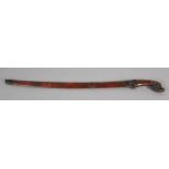 A MALAY SWORD with a curved and fullered 23½" patinated blade, carved naturalistic grip, metal bound