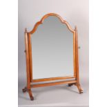 A WALNUT TOILET MIRROR, of arched outline on square framing with acorn finials and on scrolled feet,