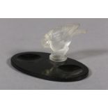 A FRENCH MOULDED OPAQUE GLASS BIRD, mounted on a black glass desk tidy of oval outline, c.1930s,