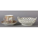 A KPM BERLIN PORCELAIN TREMBLEUSE TWO-HANDLED CUP AND SAUCER WITH RETICULATED BASKET, polychrome