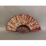 A large and vibrant 19th century scrap fan, the wood sticks, in Japanese style, dyed dull red, the