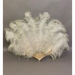 A large white ostrich feather fan, the bone sticks carved, pierced and coloured in several shades of