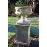 A cast urn with lower reeded body, stiff leaf socle on square plinth raised on a square pedestal