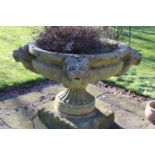 A large cast urn, circular with four lion face masks to the rim, on fluted socle to the rim, 125cm x