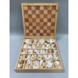 An Inuit carved chess set, the pieces carved as sea life and birds in marine tusk, held in a