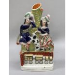 A Staffordshire pottery spill vase group of a Scotsman and girl with spaniel before a bocage and