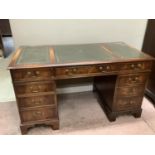 Reproduction mahogany desk having a green leather incised writing surface, three drawers across