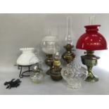 Four metal oil lamps, one retro, one with associated red shade, one glass oil lamp with bubble