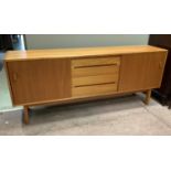 A 1970's teak sideboard having three drawers to the centre flanked by a cupboard door to either side