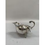 A George VI silver sauce boat with indented rim, three scalloped pad feet and foliate scroll handle,