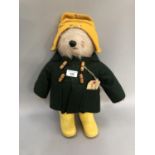 A vintage Paddington bear wearing a yellow hat, green duffle coat with label and yellow Wellington