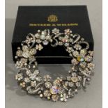 A wreath brooch by Butler and Watson foliate cluster set with foil backed paste on white base metal,