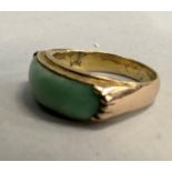 A jade dress ring, c.1950, the oblong carved cabochon with rounded terminals collet and claw set
