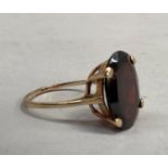 A garnet single stone dress ring in 9ct gold, the oval facetted almandine stone claw set over a fine