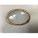 A Victorian agate brooch in 9ct gold, the oval cabochon stone collet set within a foliate and scroll