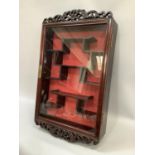 An Oriental hardwood and glazed hanging display cabinet with pierced pediment and apron