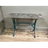 A garden table pine top on ornate wrought iron legs painted in green, the two supports joined by