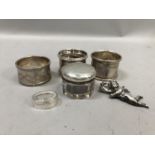 Three early 20th century silver napkin rings together with a silver topped jar, a pill box and